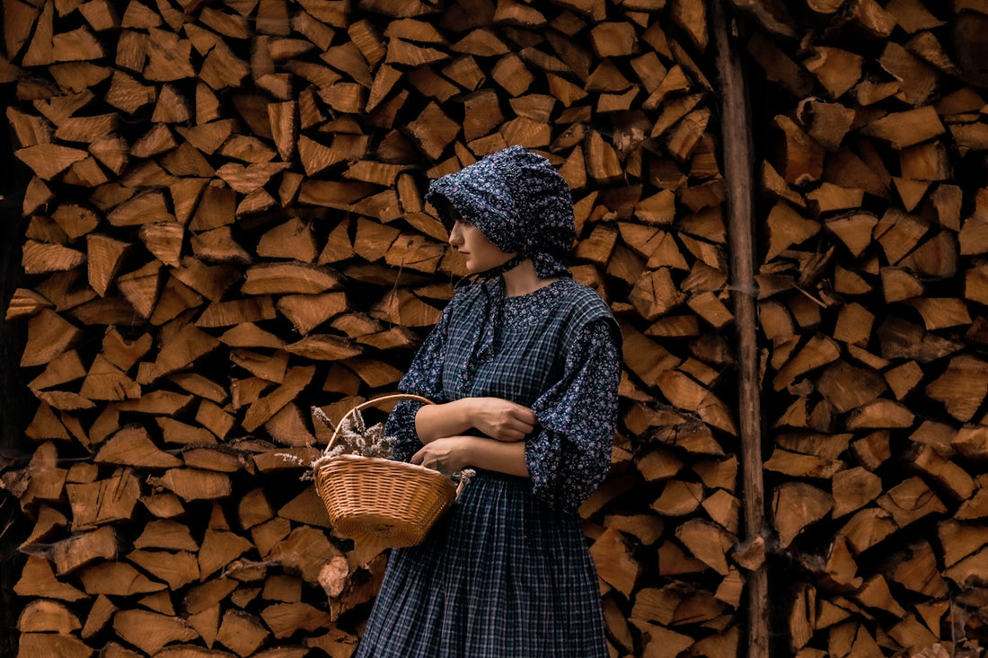 Woman in historical dress holding basket against stacked firewood