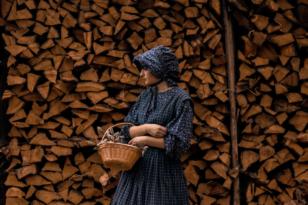 Woman in historical dress holding basket against stacked firewood